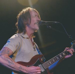 Josef Windheim singing and playing guitar on stage in a photo by TJ Martin-Lokey
